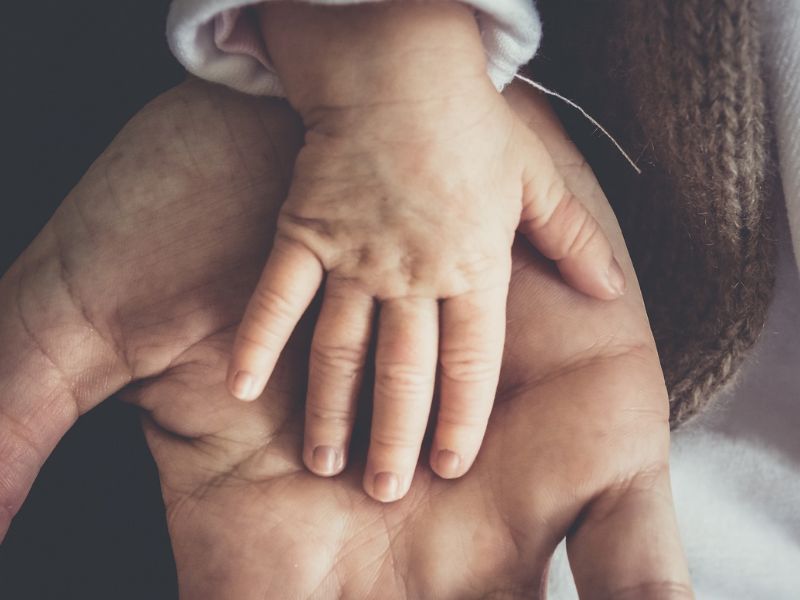 A baby's tiny hand resting on a man's hand