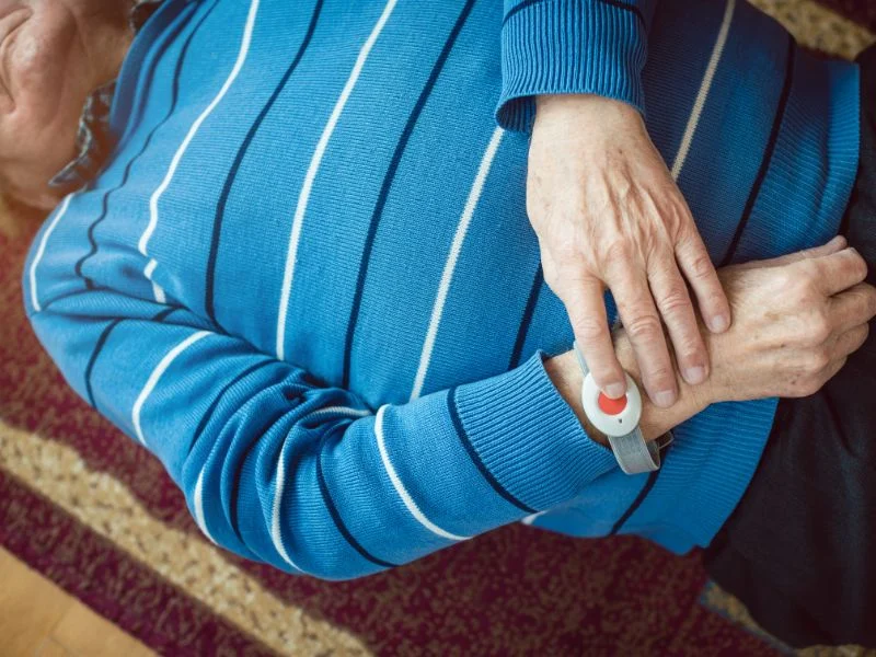 Elderly person fallen on the floor unable to get up and pushing a life alert button on their wrist