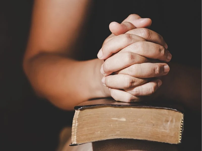 praying hands on top of the Bible
