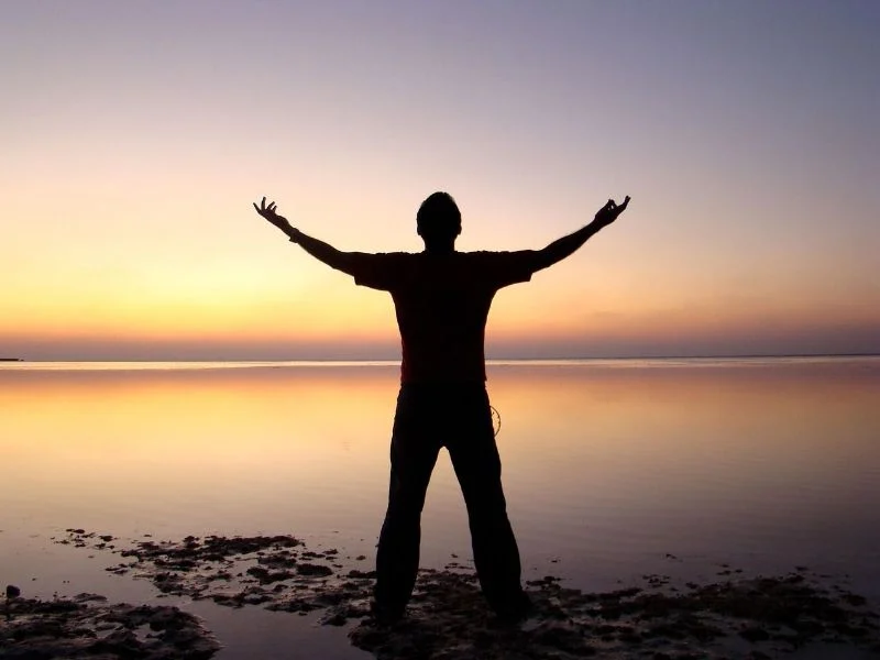 Man looking out at the sunrise with outstretched arms